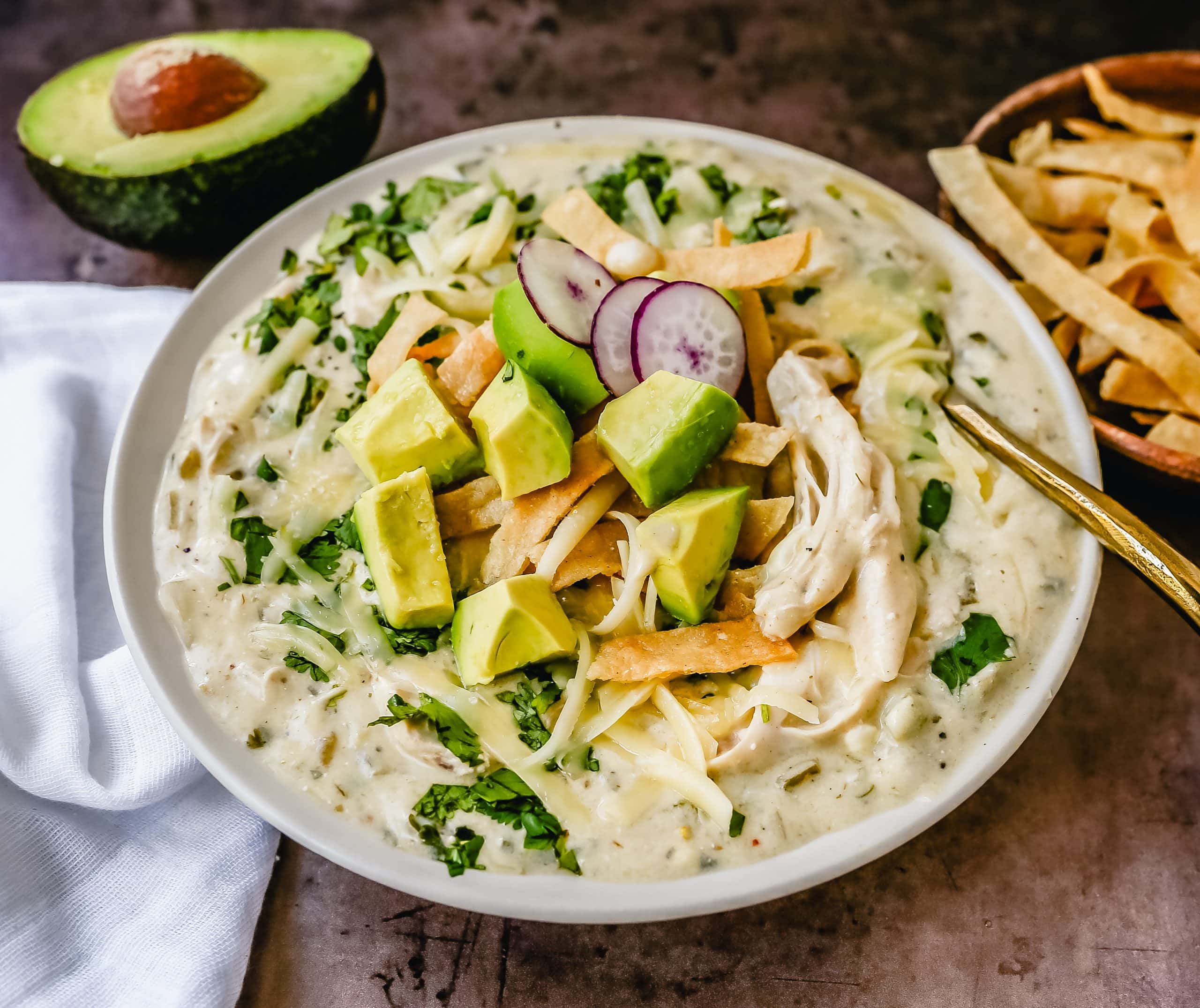 This Green Chile Chicken Enchilada Soup is made with tender chicken, green enchilada sauce, green chilies, cream cheese all in a chicken broth and topped with homemade fried tortilla strips, fresh avocado, cilantro, and Monterey Jack cheese. This is the most flavor-packed creamy green chicken enchilada soup recipe.
