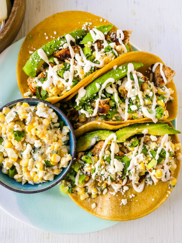 Mexican Street Corn Chicken Tacos Marinated grilled chicken with a homemade street corn salsa, fresh avocado, cotija cheese, and spiced Mexican crema. These tacos will become a family favorite in no time at all! www.modernhoney.com #taco #tacos #mexicanfood #chickentacos